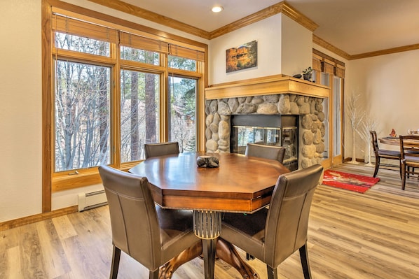 A dining area with a large wooden table, leather chairs, a stone fireplace, and large windows with a view of trees. - Forest-view Gem 2 Mi to Diamond Peak Ski Resort! (Incline Village)
