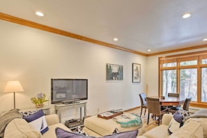 A living room with a television, a dining table, and a window with a view of trees. - Incline Village Townhome w/ Forest-view Deck (Incline Village)