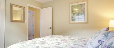 A bedroom with a floral bedspread, a framed picture on the wall, and a door leading to another room.
