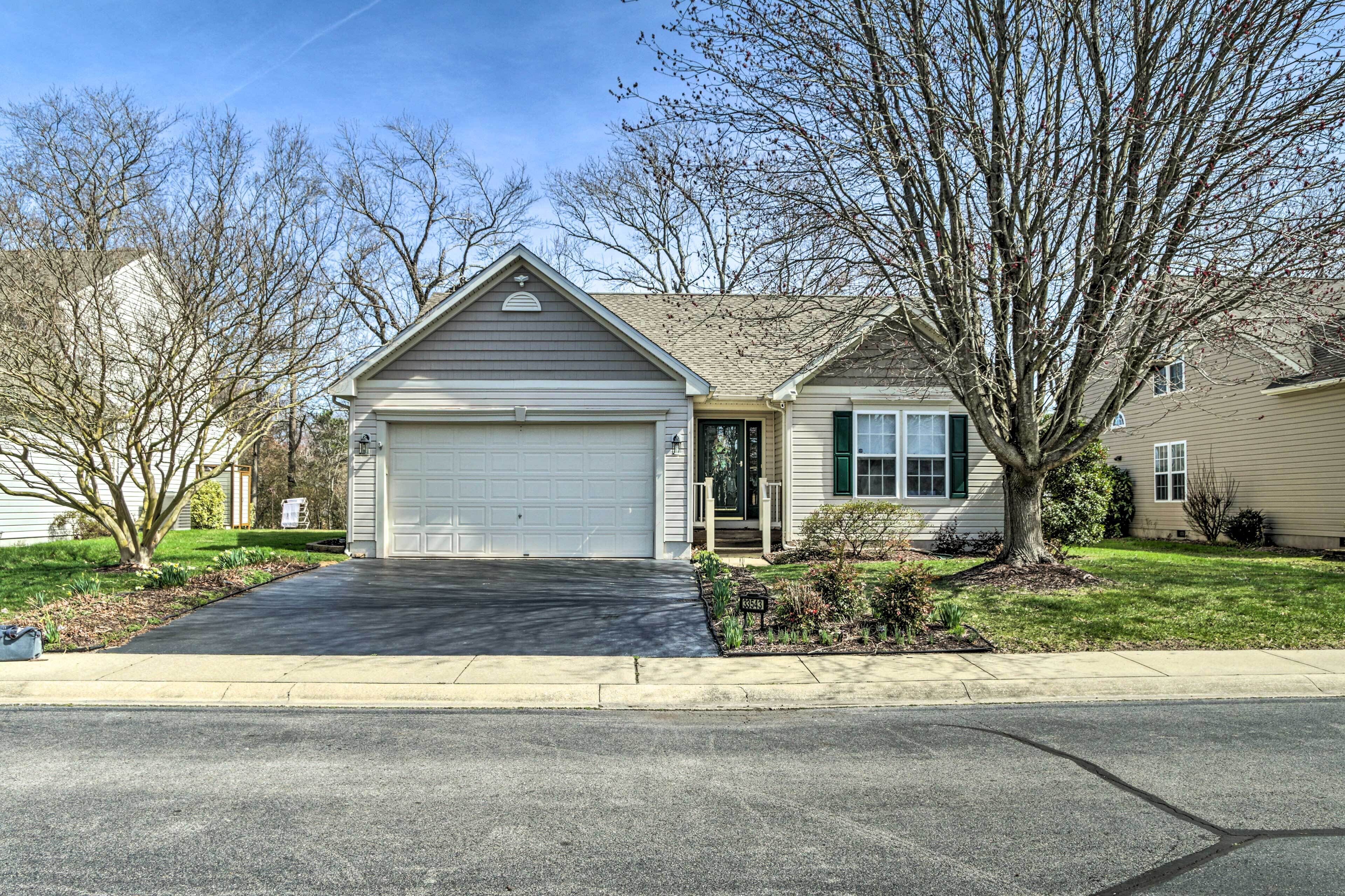 A single-story house with a garage, a front yard with a tree, and a clear sky.