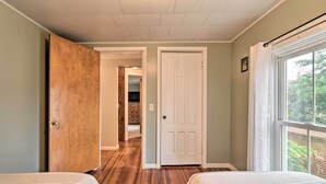 A bedroom with two beds, wooden flooring, a white door, and a window with a view of greenery.