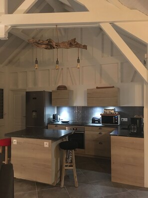 A kitchen with a central island, wooden cabinets, a stainless steel refrigerator, a microwave, and hanging pendant lights. - Villa Coco Câline, 2 suites, infinity pool (Capesterre-de-Marie-Galante)