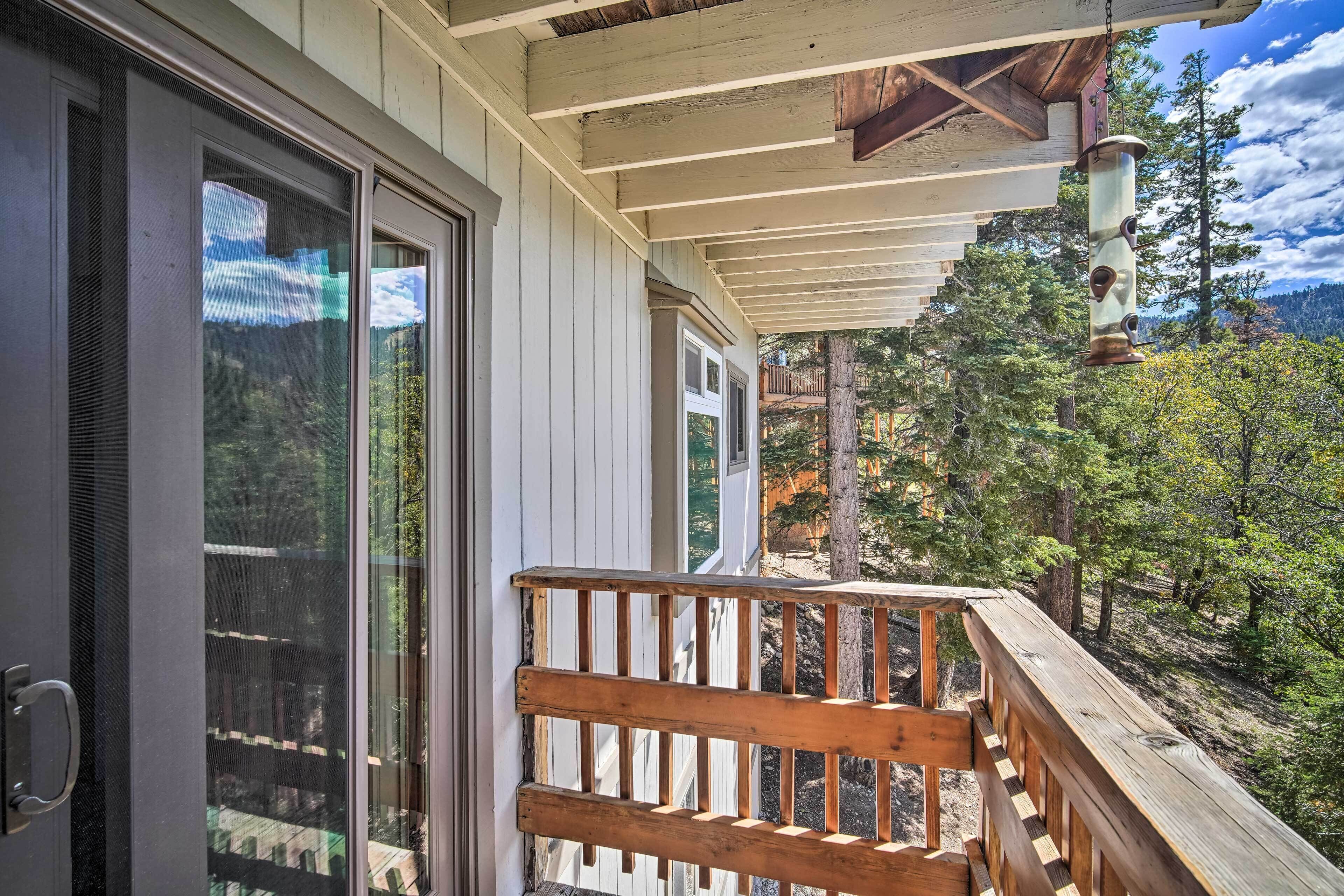 Une terrasse en bois dotée d’une rambarde, qui offre une vue sur une zone boisée avec des arbres et une montagne en arrière-plan.