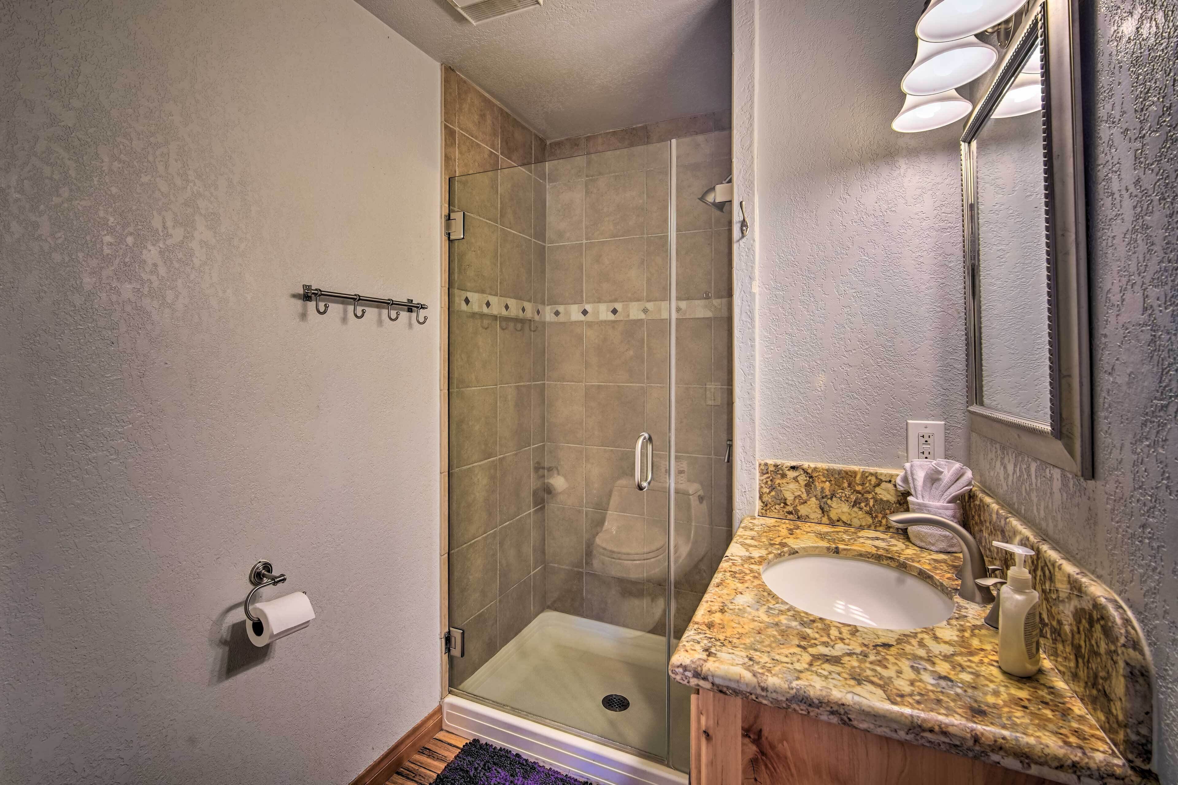 Baño con ducha envuelta en vidrio, lavamanos con encimera de mármol y retrete visible desde la ducha.