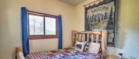 A bedroom with a wooden headboard, a quilted bedspread, a welcome tapestry, and a small bedside table.