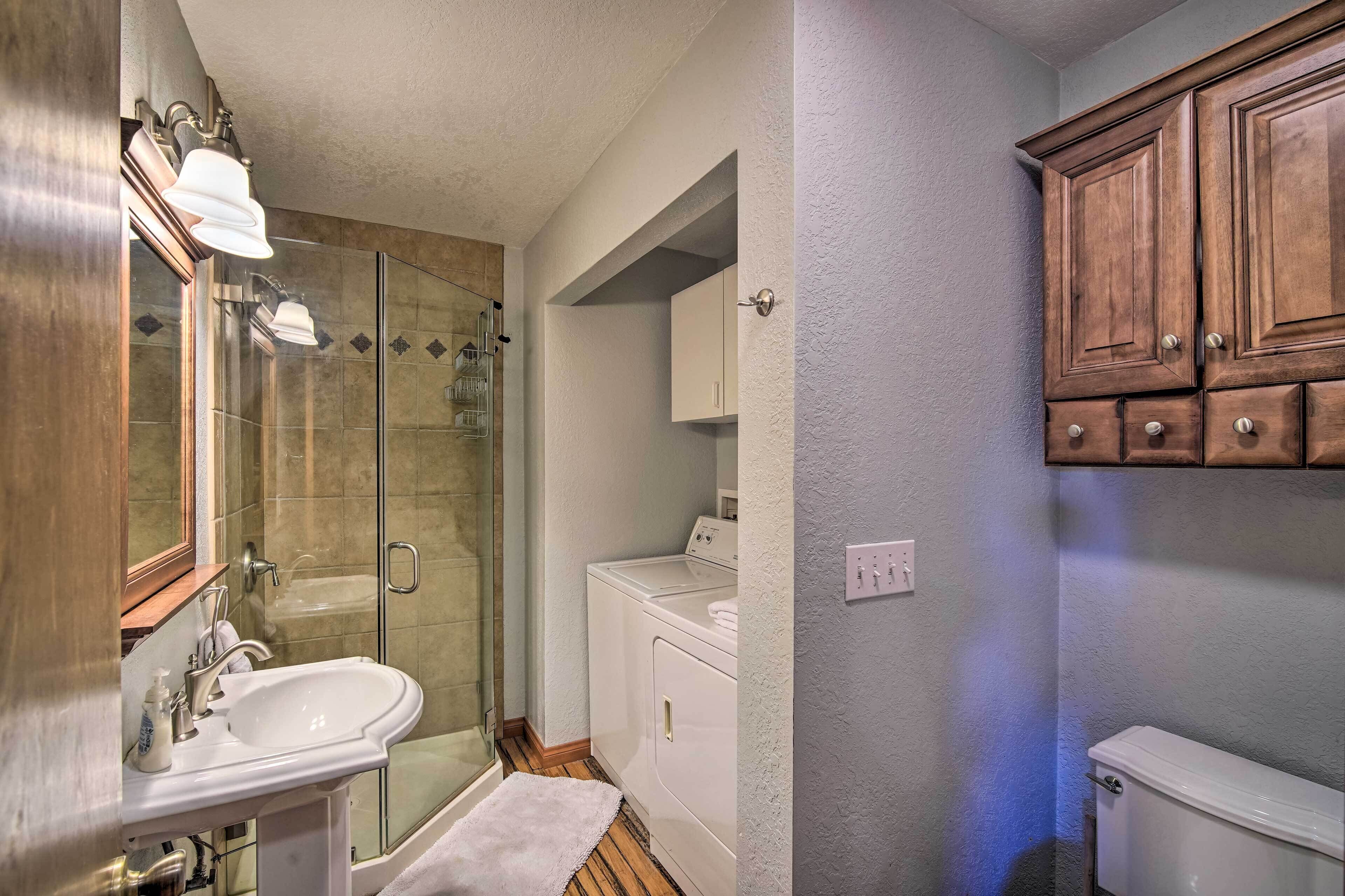 A bathroom with a glass shower enclosure, a white sink, wooden cabinets, and a white toilet.