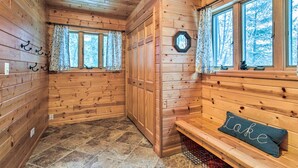 A wooden cabin interior with a stone-tiled floor, wooden walls, a bench with a pillow, and two windows with curtains. - Crandon Cabin Getaway w/ Boat Dock & Deck! (Crandon)
