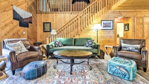 A cozy log cabin interior with a green sofa, leather armchairs, a round coffee table, and a staircase with a bear decoration. - Crandon Cabin Getaway w/ Boat Dock & Deck! (Crandon)