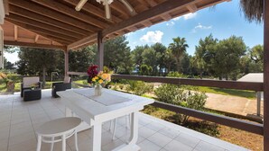 A covered patio with a white table and chairs, a ceiling fan, and a view of a landscaped garden.