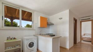 A compact kitchen with a washing machine, a small island counter, and a window overlooking greenery.