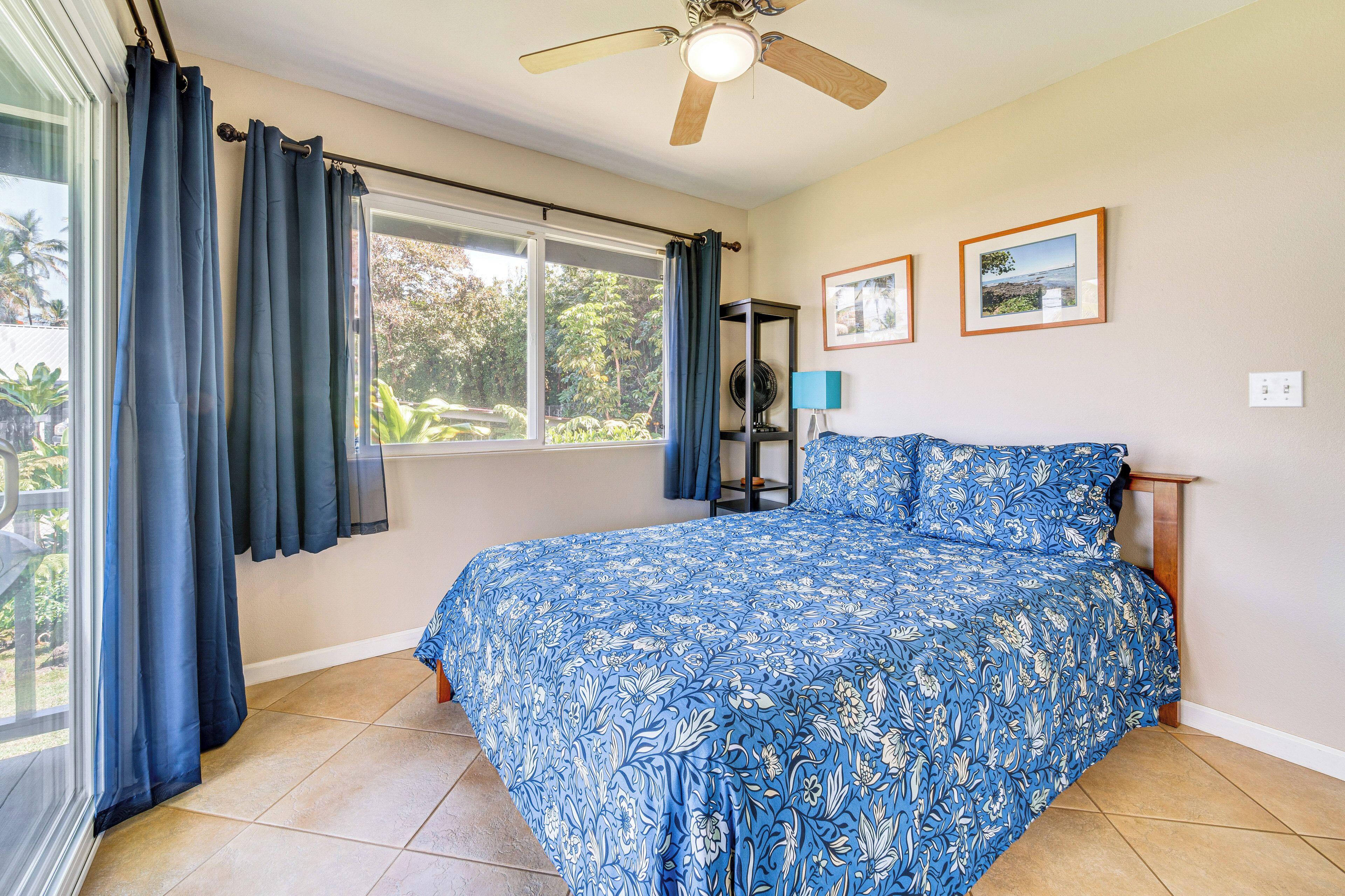 A bedroom with a large bed, a ceiling fan, a window with curtains, and two framed pictures on the wall.
