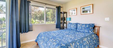 Een slaapkamer met een groot bed, een plafondventilator, een raam met gordijnen en twee ingelijste foto's aan de muur.