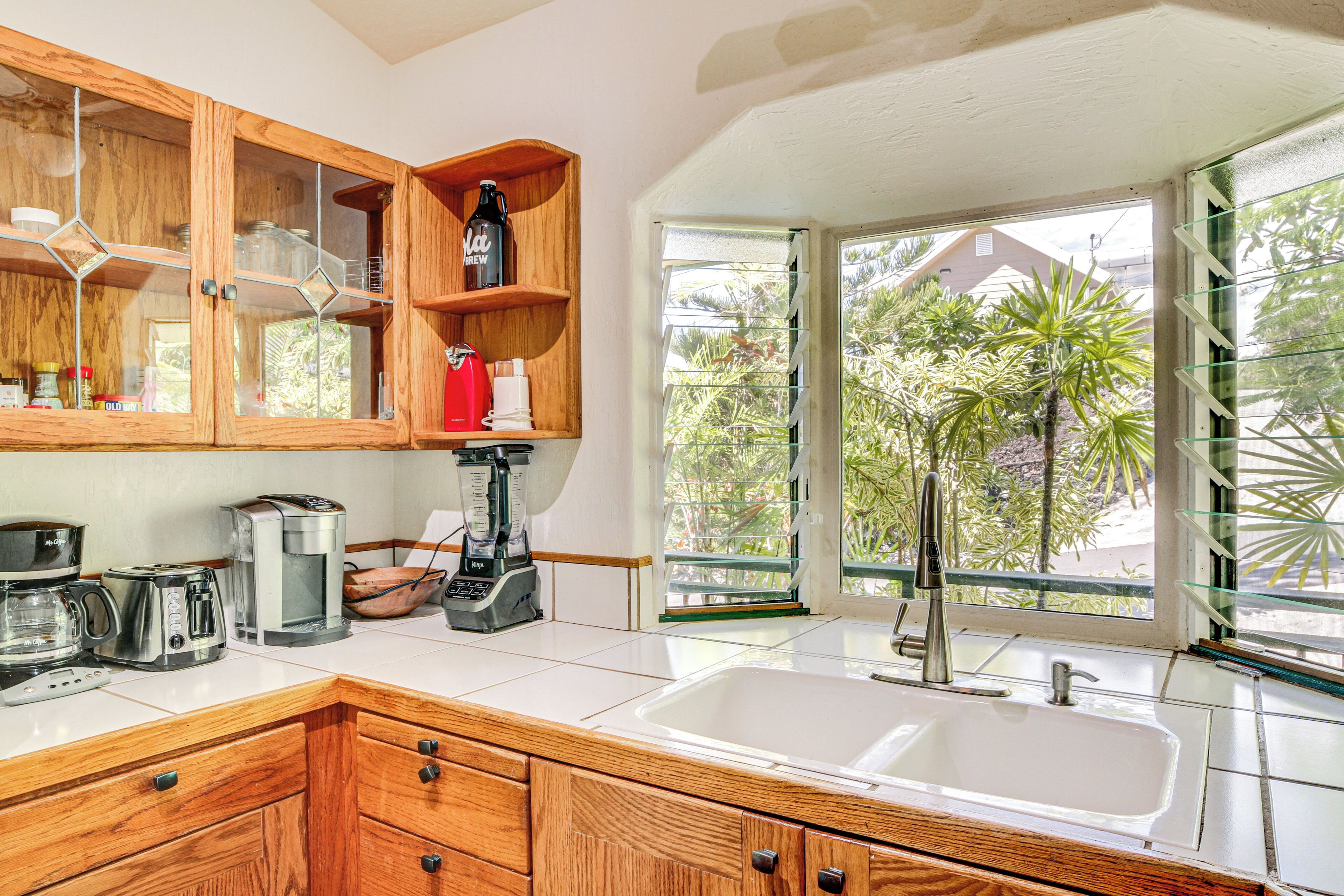 A kitchen with wooden cabinets, a coffee maker, a blender, and a large window with a view of greenery.