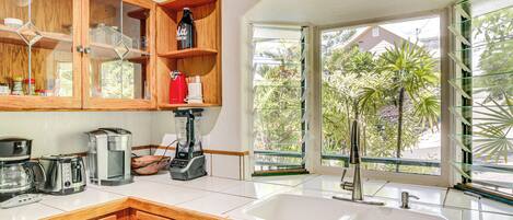 A kitchen with wooden cabinets, a coffee maker, a blender, and a large window with a view of greenery.