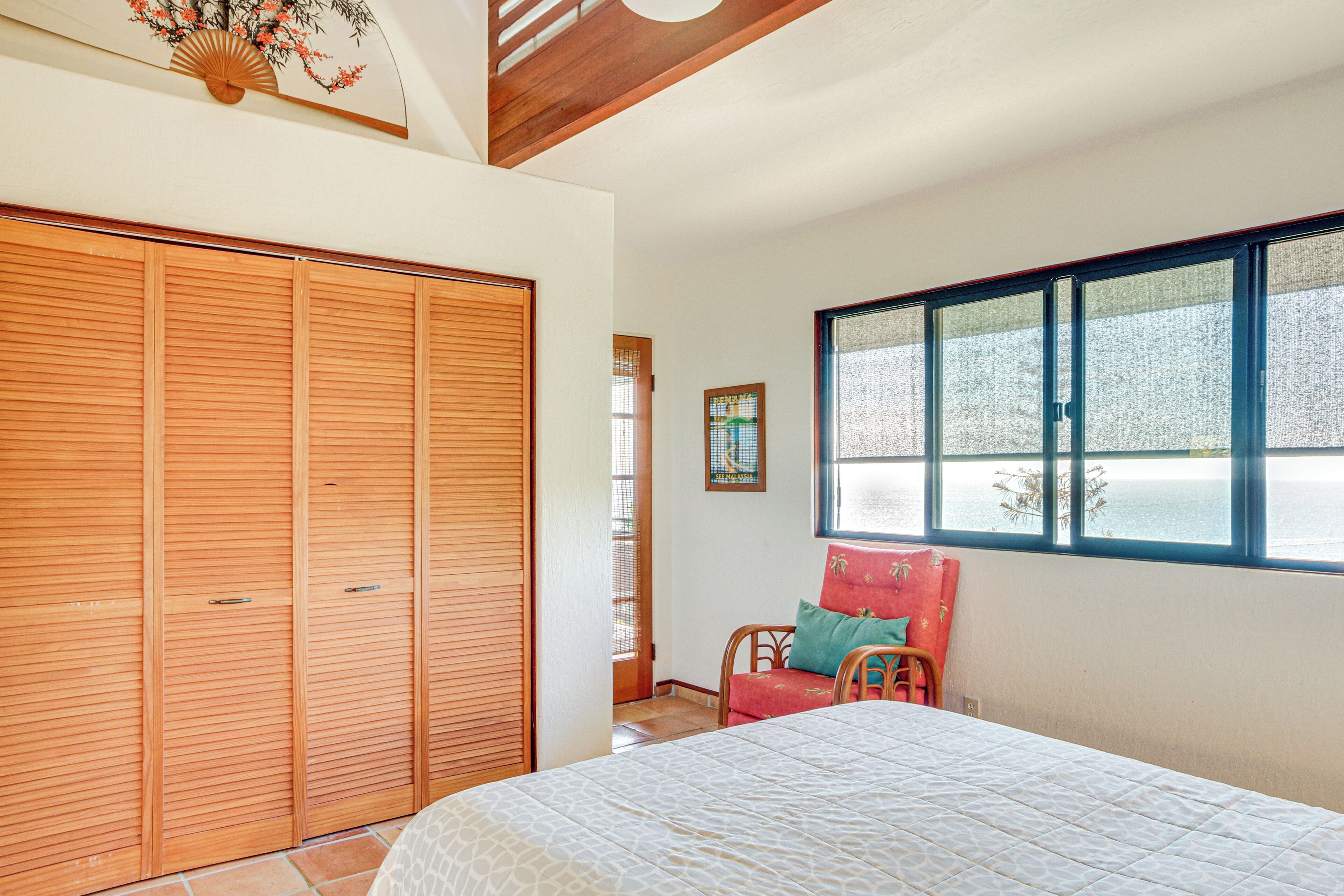 Quarto com cama grande, guarda-roupa de madeira e janela com vista para o mar.