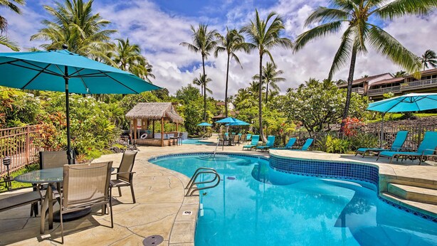 A pool area with lounge chairs, umbrellas, and a thatched-roof hut.