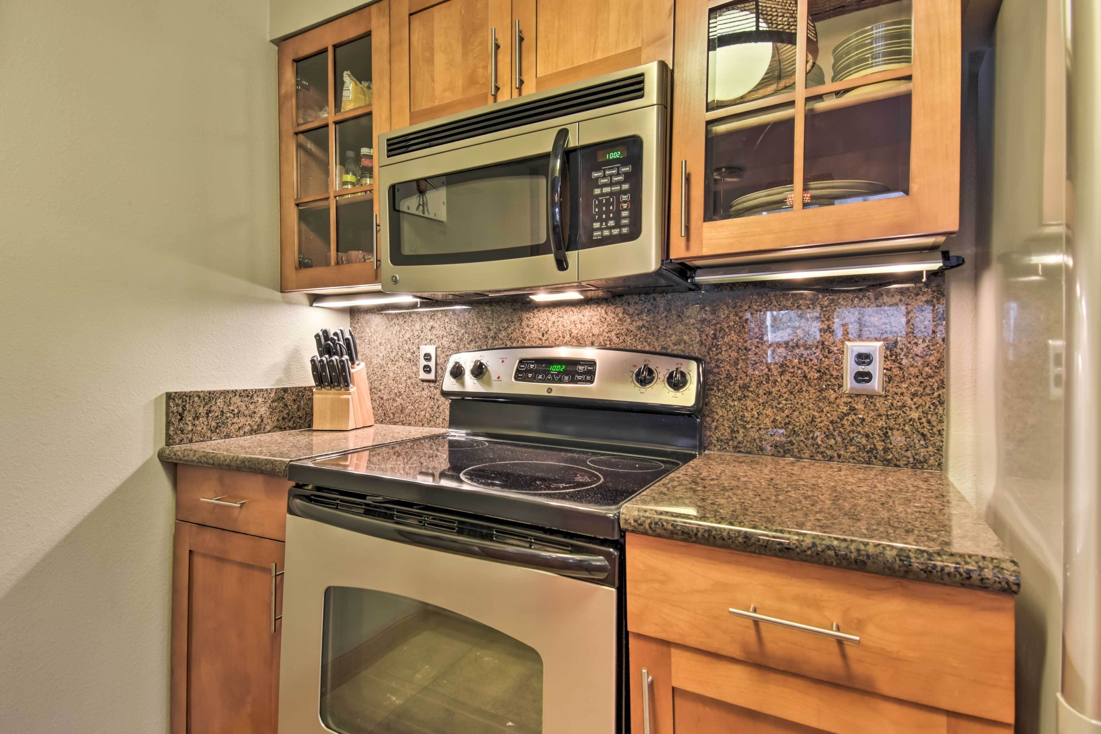 Una cocina equipada con microondas, estufa, horno, encimera de granito, armarios de madera y un escurreplatos.