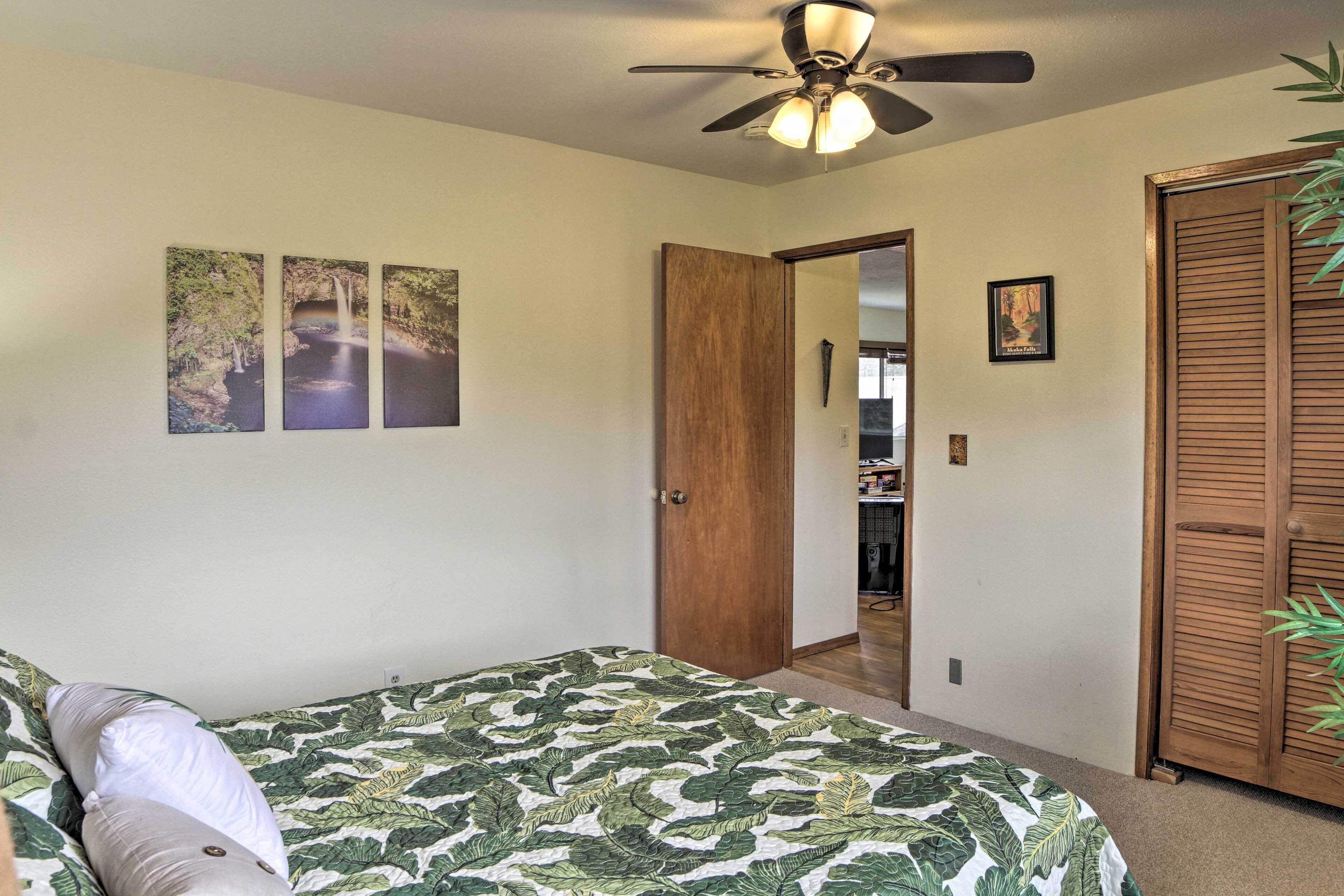 A bedroom with a bed, a ceiling fan, a door, and a wall with three framed pictures.