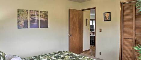 A bedroom with a bed, a ceiling fan, a door, and a wall with three framed pictures.