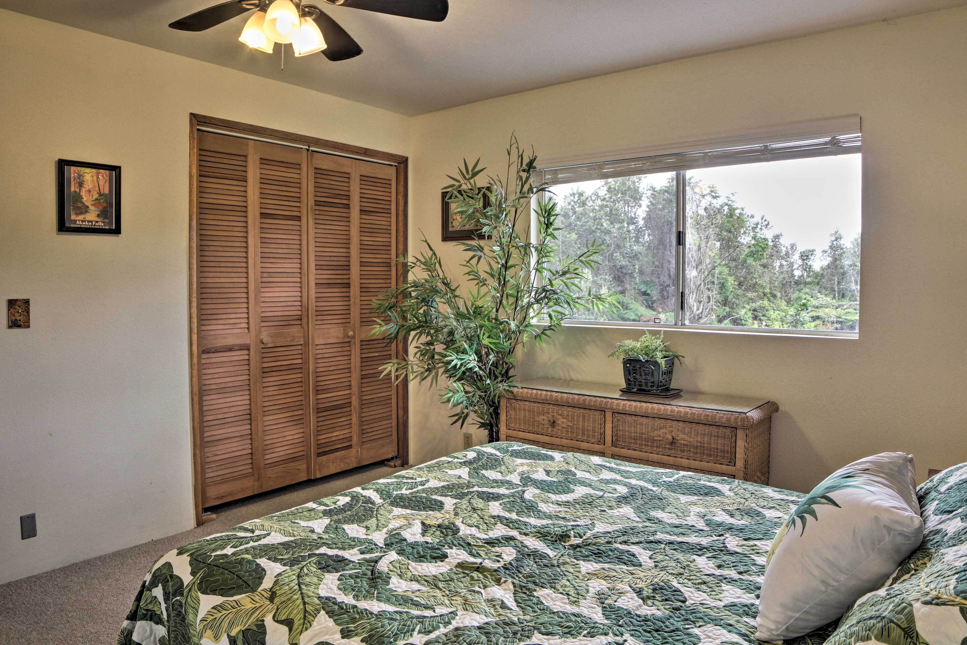 A bedroom with a bed, a window with a view of trees, a ceiling fan, and a wooden wardrobe.