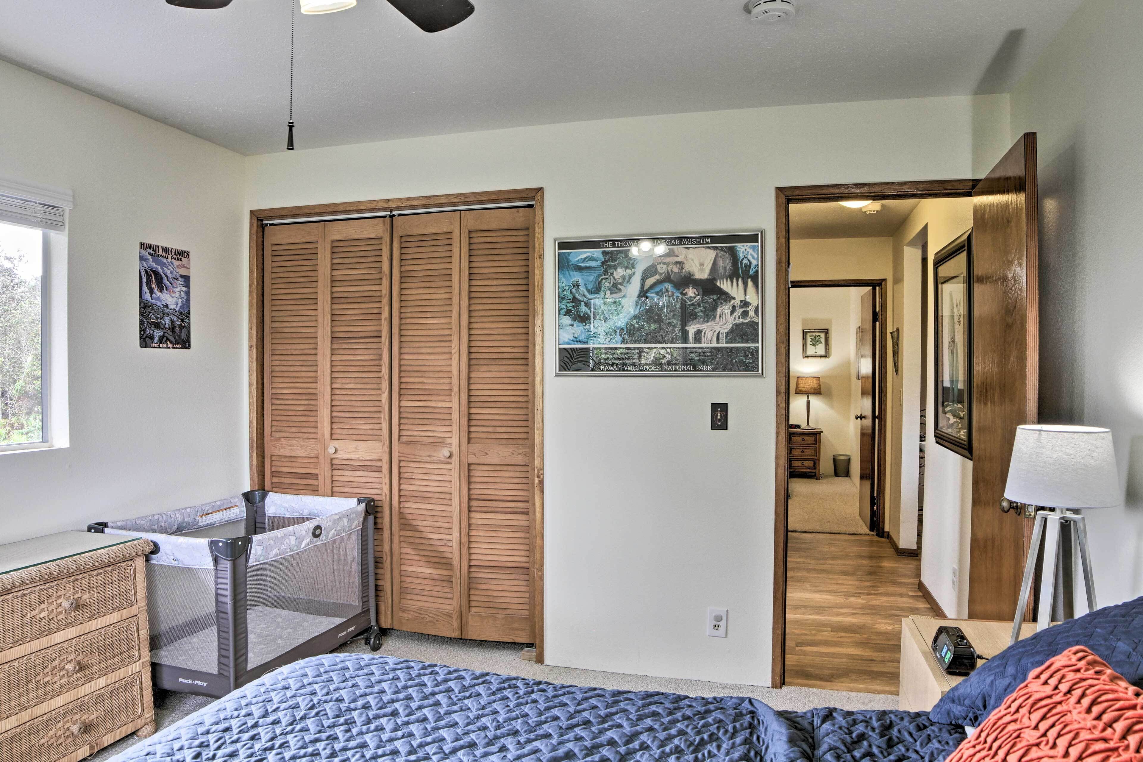 A bedroom with a bed, a crib, a wooden wardrobe, and a poster of Hawaii Volcanoes National Park.