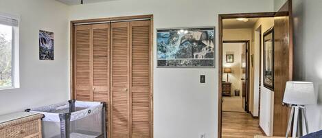 A bedroom with a bed, a crib, a wooden wardrobe, and a poster of Hawaii Volcanoes National Park.
