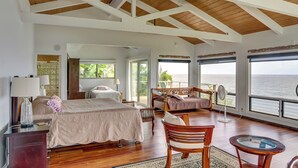 A spacious bedroom with a large bed, a sitting area with a chair and table, and a balcony with a view of the ocean. - Hilo Home w/ Private Deck + Stunning Ocean Views! (Hilo)