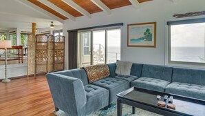 A modern living room with a grey sectional sofa, a coffee table, and a view of the ocean through large windows. - Hilo Home w/ Private Deck + Stunning Ocean Views! (Hilo)