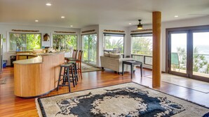 A spacious living area with a wooden bar, a sofa, and a dining set. - Hilo Home w/ Private Deck + Stunning Ocean Views! (Hilo)