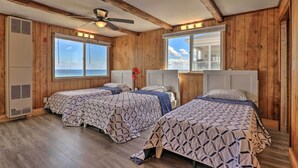 A room with two beds, wooden walls, large windows, and a ceiling fan. - Charming Oceanfront Home on Salisbury Beach (Salisbury)