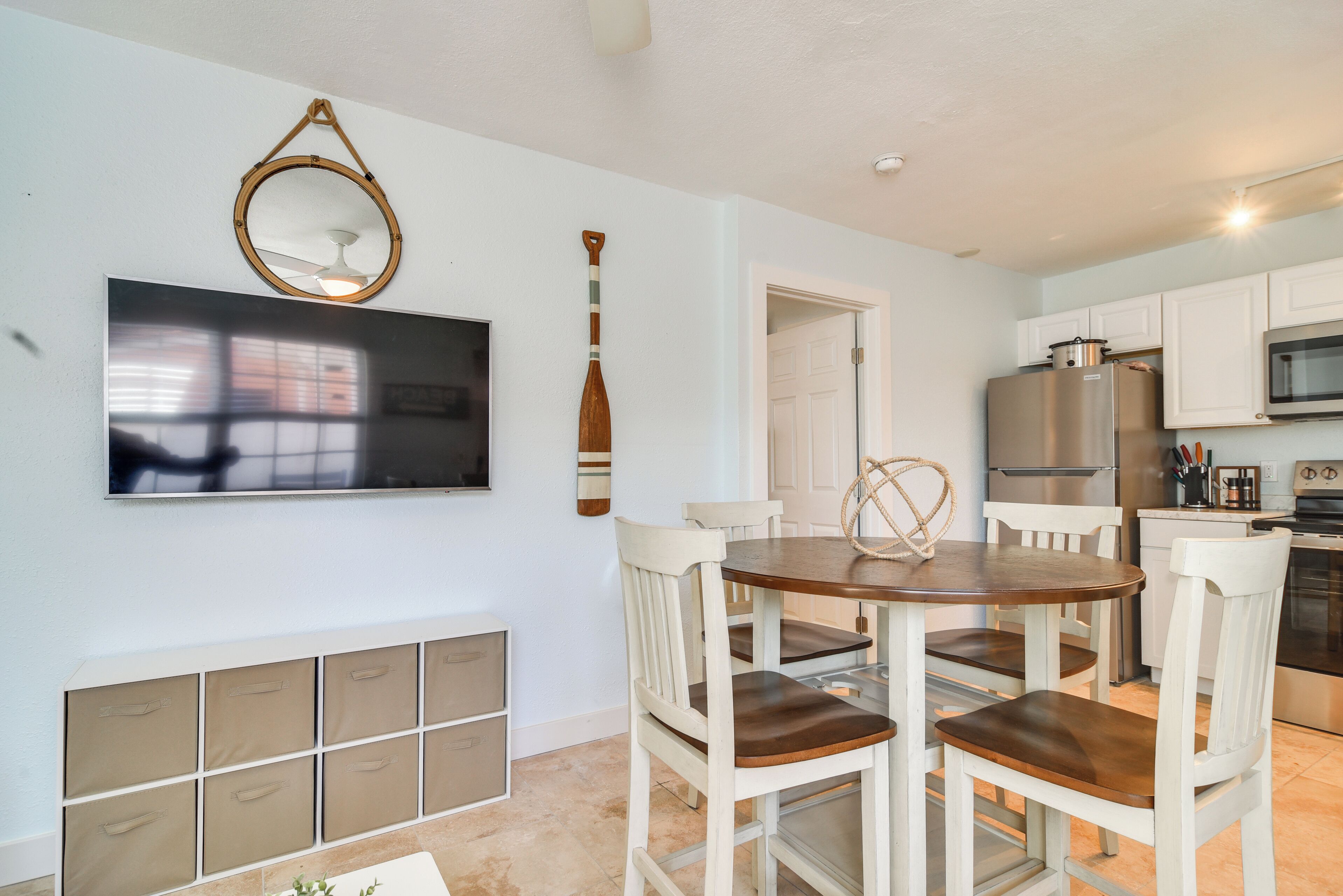 A modern kitchen with white cabinets, a stainless steel refrigerator, and a flat-screen TV mounted above the counter.