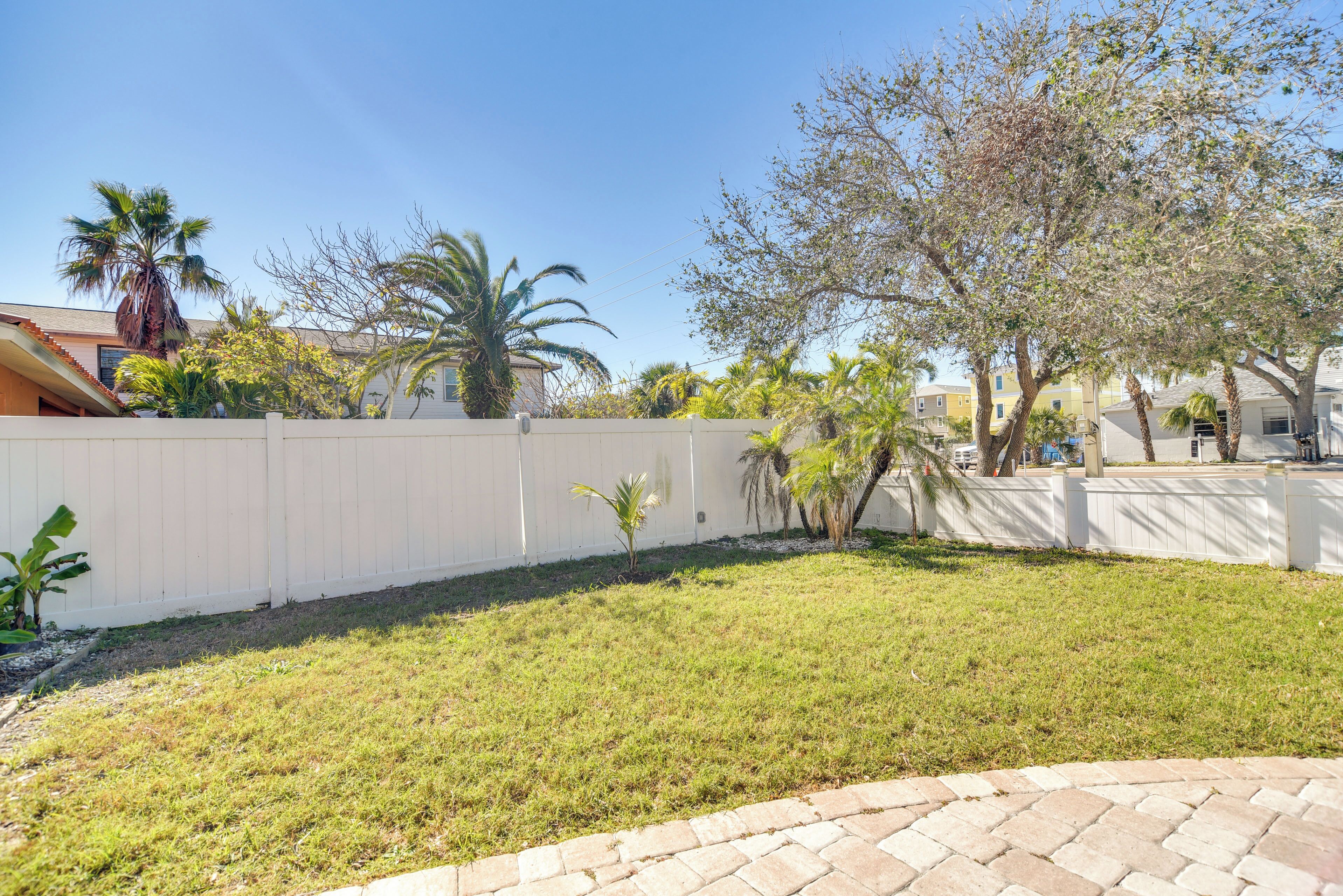 A backyard with a white fence, grass, and palm trees.