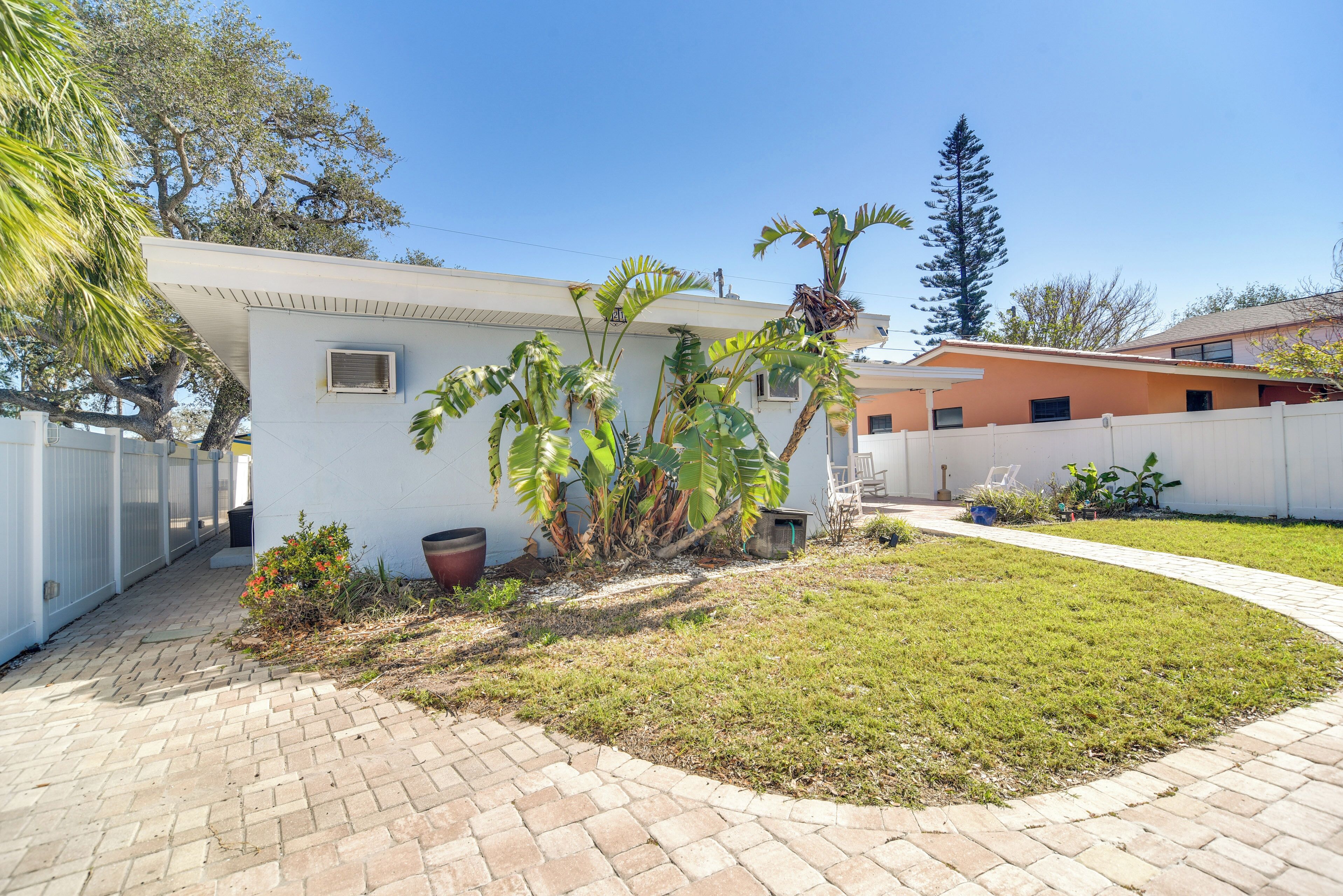 A residential property with a paved driveway, a white exterior, and a small garden with palm trees and a potted plant.