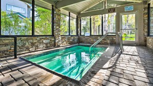 Una piscina cubierta al aire libre con paredes de piedra y suelo de ladrillo, rodeada de árboles y una casa.