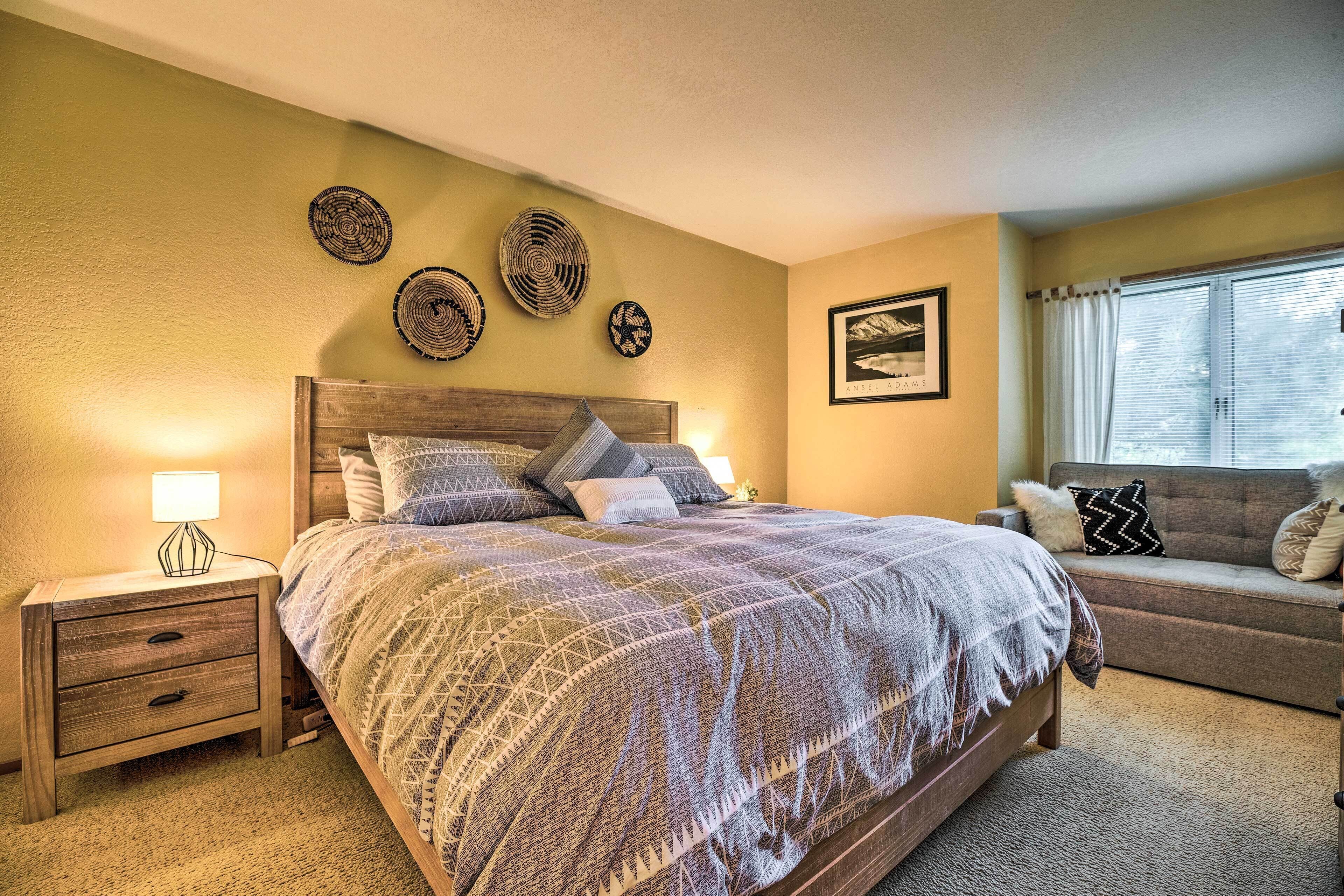 A bedroom with a large bed, a nightstand with drawers, a sofa, and a wall with decorative plates.