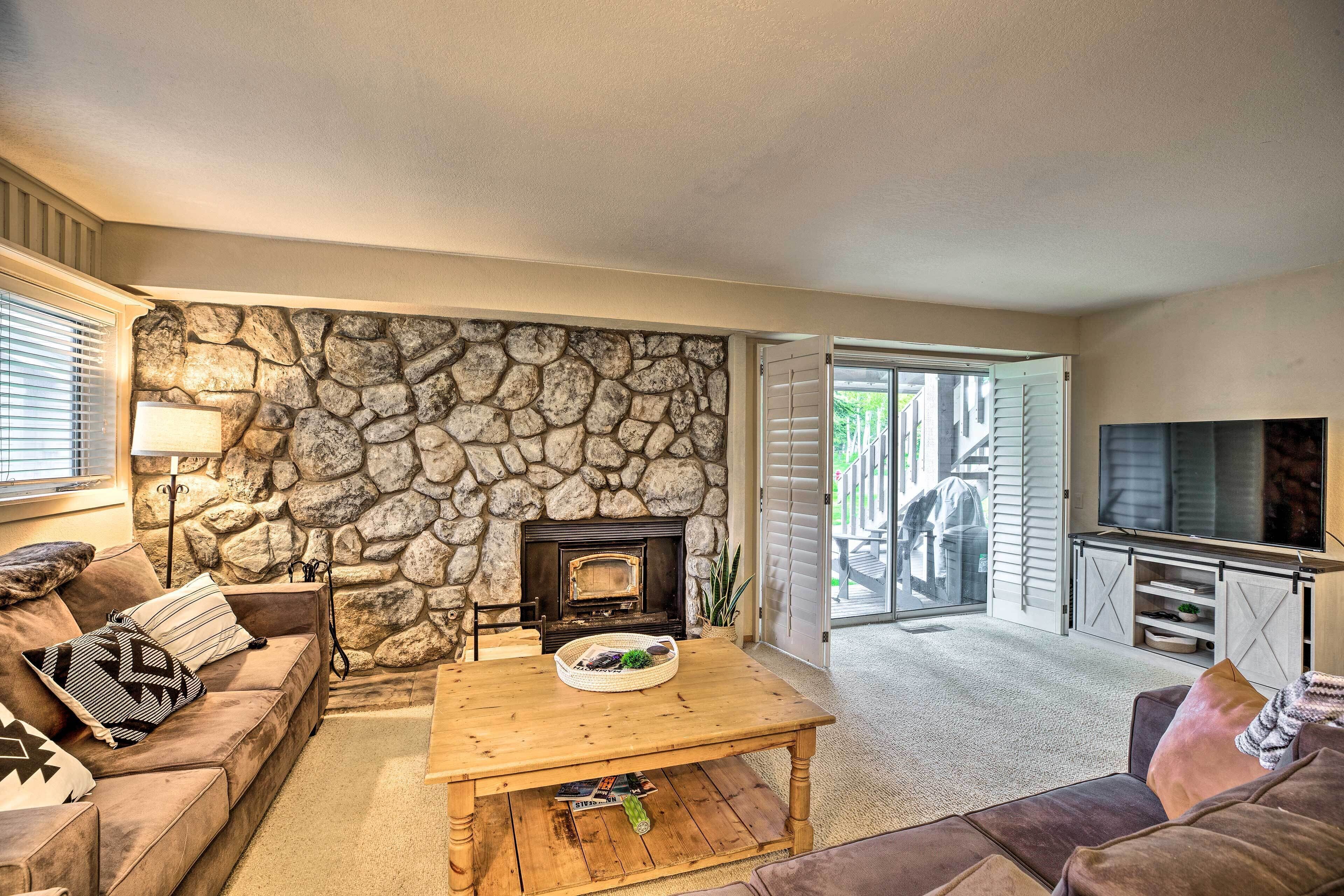 A cozy living room with a stone wall, a fireplace, a wooden coffee table, and a television.