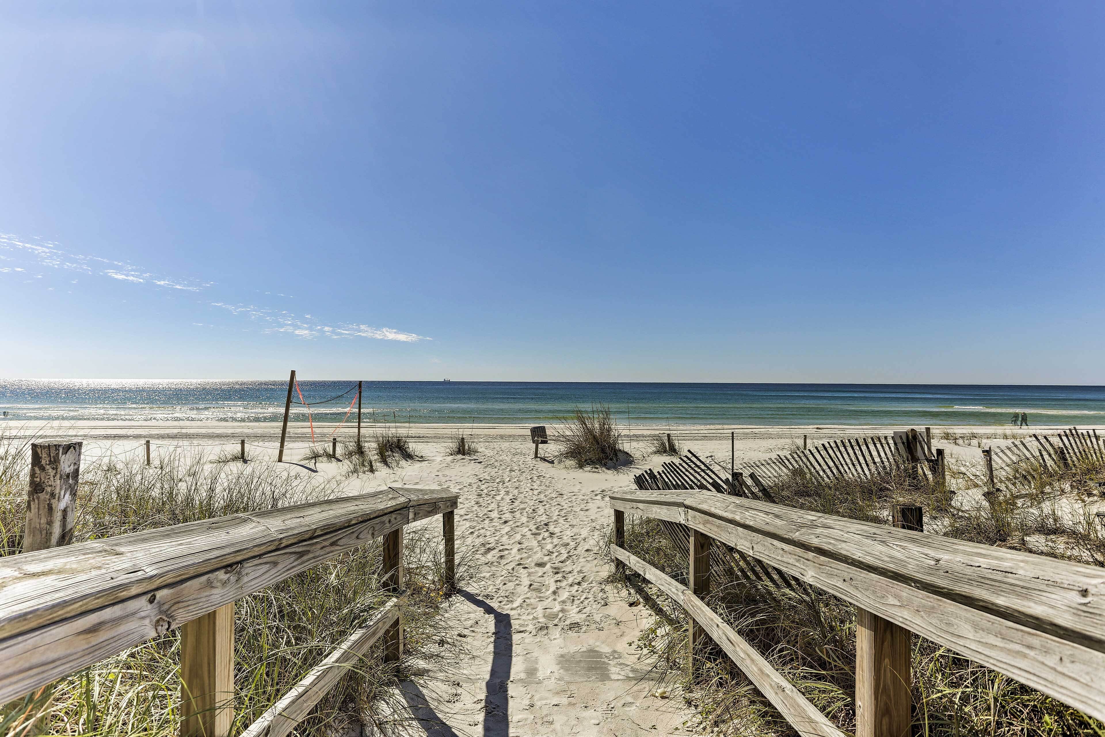 Una passerella di legno che conduce a una spiaggia sotto un cielo sereno.