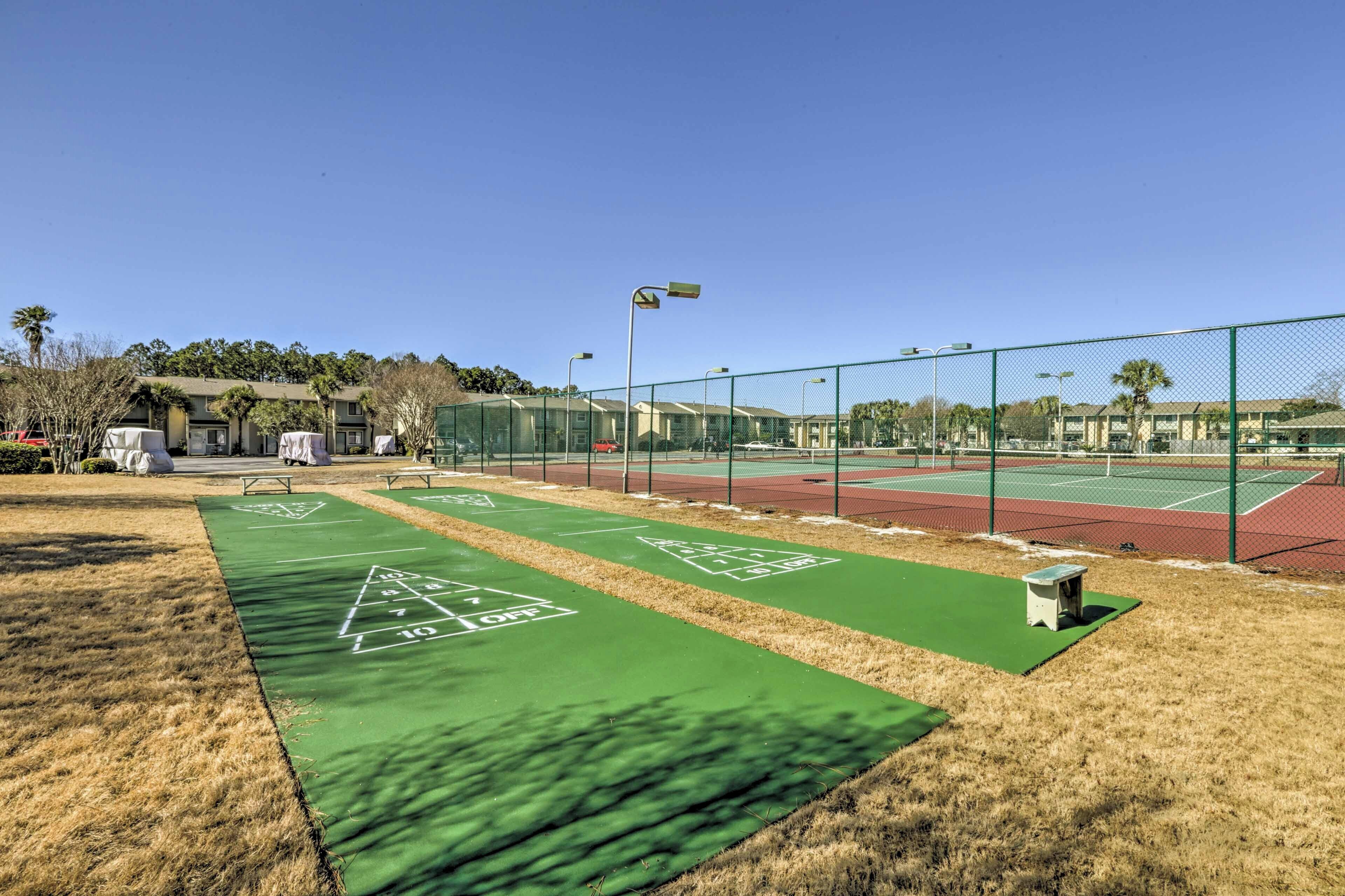 A tennis court with a green surface, a fence, and a small bench.