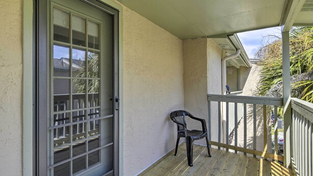 A wooden balcony with a metal railing, a sliding glass door, and a black plastic chair. - Walk to Beach: Modern PCB Townhome w/ Patio (Panama City Beach)
