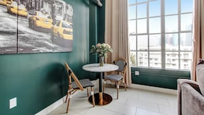 Ein Zimmer mit grüner Wand, einem großen Fenster, einem runden Tisch mit Stühlen und einem Gemälde von Taxis.