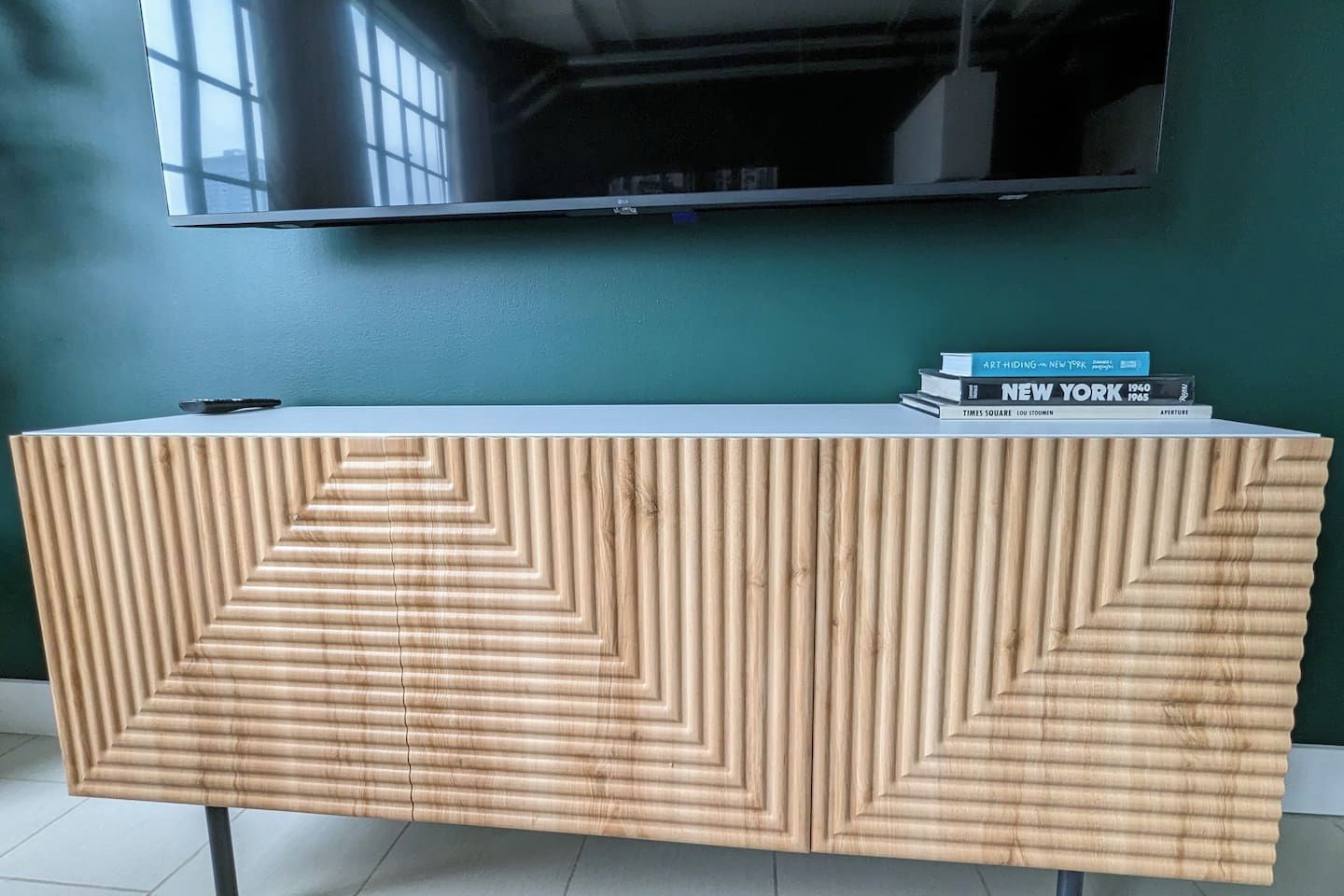 A wooden console table with a geometric pattern, a flat-screen TV mounted above, and a stack of books on top.
