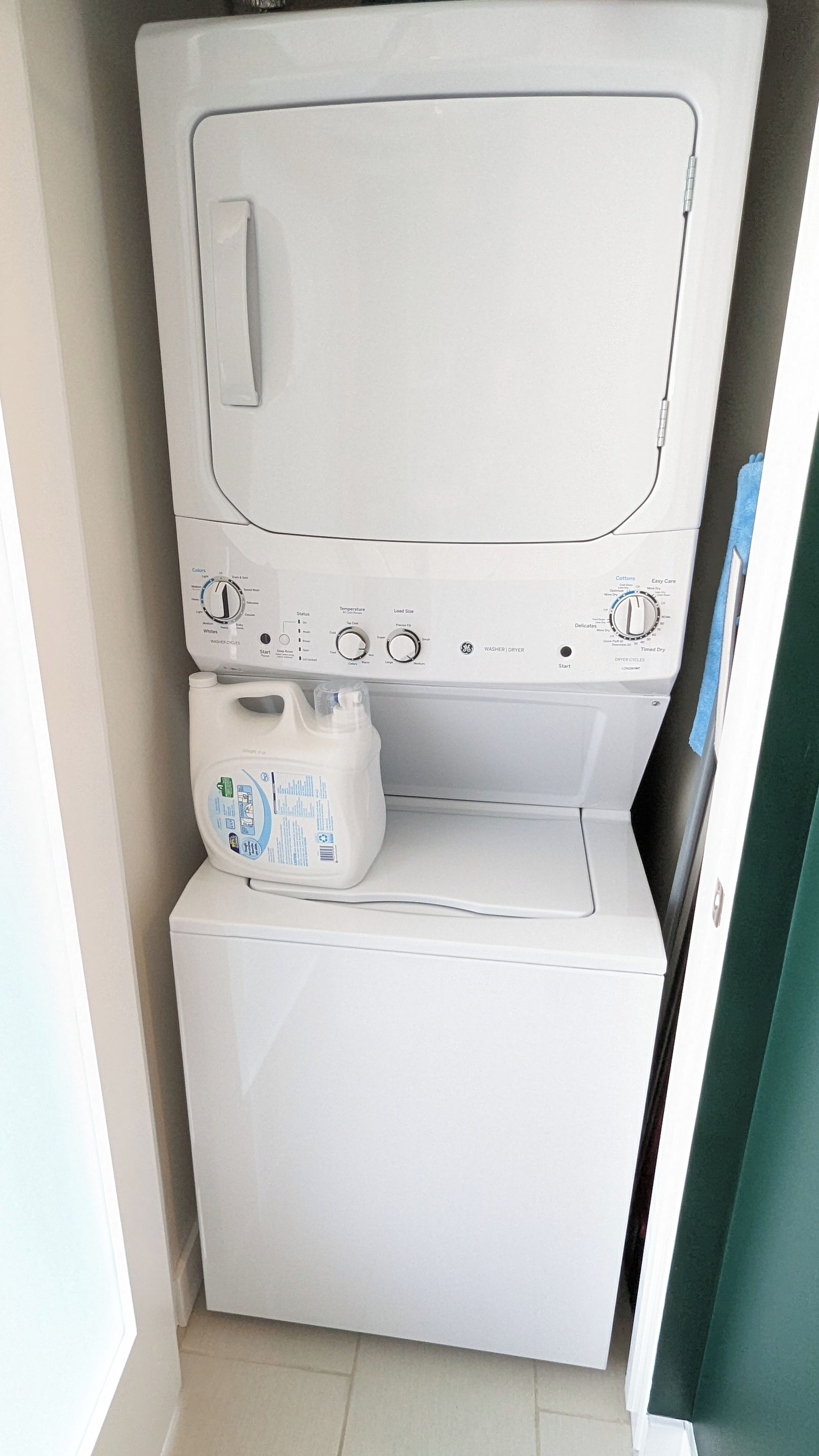 Una lavadora compacta de carga frontal, blanca, con panel de control, dispensador de detergente y una unidad secadora más pequeña debajo.