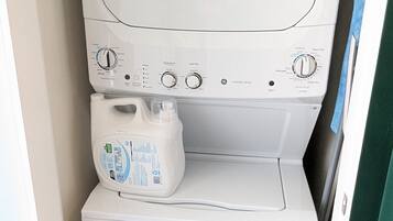 Una lavadora compacta de carga frontal, blanca, con panel de control, dispensador de detergente y una unidad secadora más pequeña debajo.