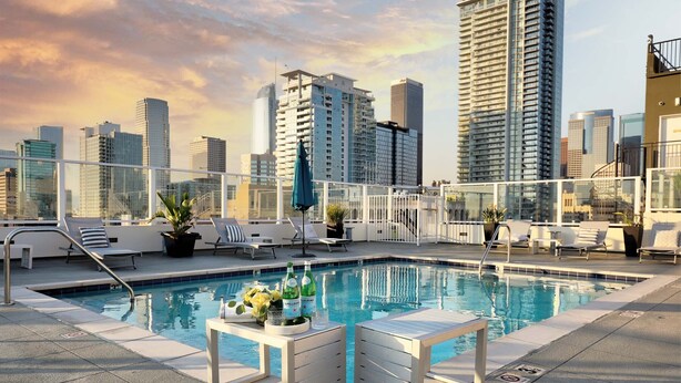 Ein Dachpool mit Liegestühlen und Bar, umgeben von hohen Gebäuden.