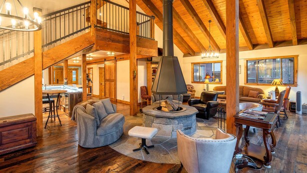 A spacious living area with a stone fireplace, wooden beams, a staircase, and a cozy seating arrangement. - 2 Blocks to Lake Tahoe! Group Gem w/ Hot Tub (Incline Village)