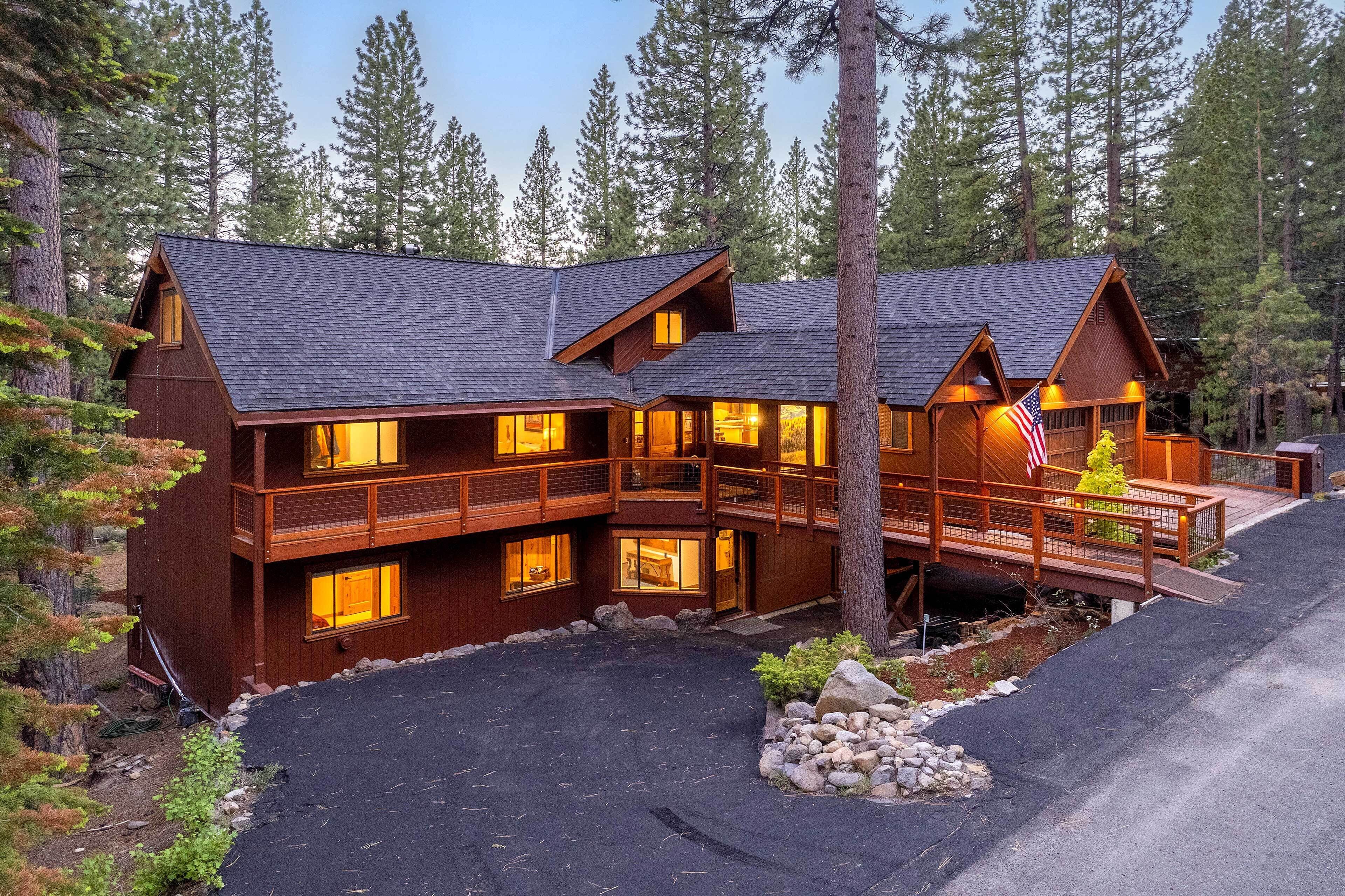 A two-story log cabin with a balcony and a deck, surrounded by trees.