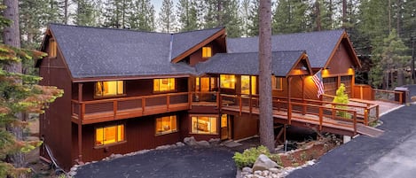 A two-story log cabin with a balcony and a deck, surrounded by trees.