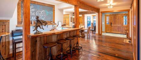 A rustic bar area with wooden beams, a chalkboard with writing, and a horse sculpture.
