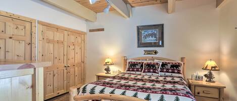 Un dormitorio acogedor con techo de madera, una cama con colcha festiva, dos mesitas de noche con lámparas y un cuadro enmarcado en la pared.