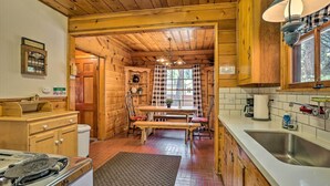 A wooden cabin-style kitchen with a wooden table, chairs, and a bench. There is a sink, a stove, and a refrigerator. - Big Bear Lake Cabin ~ 4 Mi Snow Summit Ski Resort (Big Bear Lake)